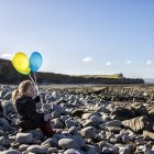 Girl on beach holding balloons — Stock Photo