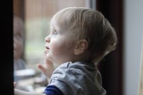 Дитячий хлопчик дивиться з вікна — стокове фото