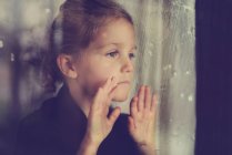 Chica mirando a través de ventana húmeda - foto de stock