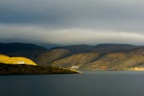 Paesaggio con lago, colline e cielo coperto — Foto stock