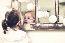 Chica en gafas de vista mirando en el espejo - foto de stock