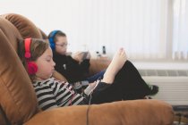 Hermanos sentados en un sofá con auriculares - foto de stock