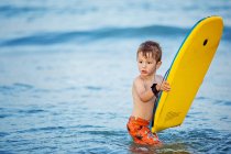 Хлопчик стоїть у морі з дошкою для серфінгу — стокове фото