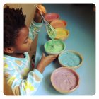 Little girl preparing rainbow cake — Stock Photo