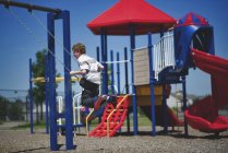 Rapaz balançando no balanço no parque infantil — Fotografia de Stock