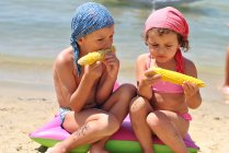 Девочка и мальчик едят сладкую кукурузу на пляже — стоковое фото