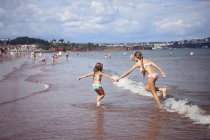 Irmãs de mãos dadas correr ao longo da praia — Fotografia de Stock