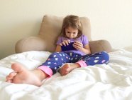 Девушка лежит в постели играет на смартфоне — стоковое фото