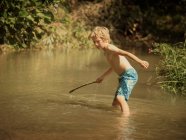 Garçon dans ruisseau tenant bâton — Photo de stock