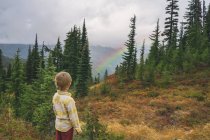 Мальчик стоит на горе и смотрит на радугу — стоковое фото