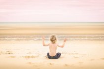 Boy sitting on beach and meditating — Stock Photo