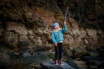 Chica de pie en la roca y la celebración de palo - foto de stock