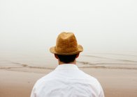 Чоловік у солом'яному капелюсі на пляжі дивиться на — стокове фото