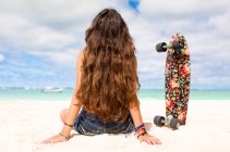 Ragazza seduta sulla spiaggia di sabbia con skateboard — Foto stock