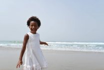 Chica de pie en la playa riendo de la cámara - foto de stock