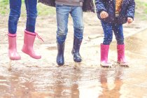 Діти в чоботях у Веллінгтоні стрибають у калюжу — стокове фото