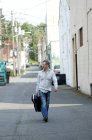 Man with guitar case walking down alley — Stock Photo