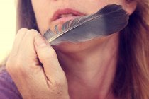 Woman holding feather close to face — Stock Photo