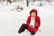 Хлопчик сидить у снігу зі сніжною кулею — стокове фото
