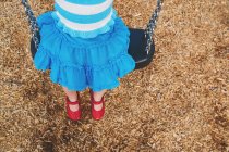 Девушка сидит на качелях в парке на детской площадке — стоковое фото