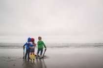 Дети стоят на пляже с лопатами — стоковое фото