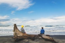 Chicos sentados en madera a la deriva en la playa - foto de stock