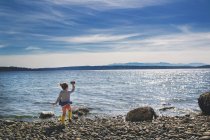 Chica lanzando roca al mar - foto de stock