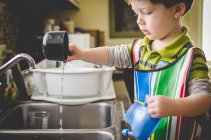 Boy playing with measuring cups and water — Stock Photo