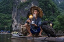 Cormorant fisherman on raft holding lantern — Stock Photo