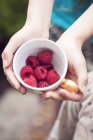 Girl holding cup with raspberries — Stock Photo