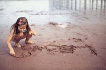 Fille écrit sur le sable — Photo de stock