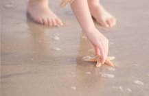 Girl picking up starfish — Stock Photo