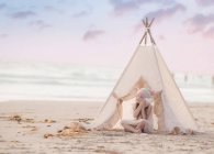 Menina sentada em wigwam na praia — Fotografia de Stock