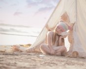 Menina sentada em wigwam na praia — Fotografia de Stock