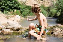 Хлопчик сидить на скелі в річці — стокове фото