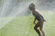 Girl playing in water sprinklers — Stock Photo