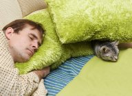 Чоловік спить на дивані з кішкою — стокове фото