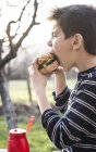 Мальчик ест гамбургер в саду — стоковое фото