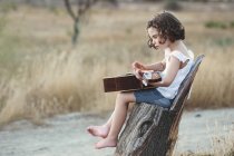 Дівчина сидить у полі граючи на гітарі — стокове фото