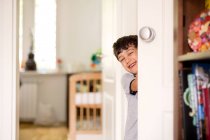 Улыбающийся мальчик, подглядывающий за дверью — стоковое фото