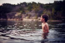 Niño de pie en el lago al atardecer - foto de stock