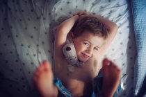 Boy lying on bed with cuddly toy — Stock Photo