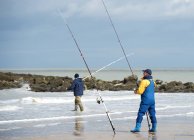 Men standing on beach fishing — Stock Photo