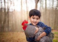 Niño sosteniendo gallo - foto de stock