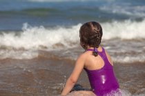 Девушка, сидящая на пляже у кромки воды — стоковое фото