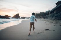 Junge läuft bei Sonnenuntergang am Strand entlang — Stockfoto