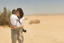 Мать, стоящая в пустыне, несет сына — стоковое фото