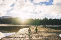 Boys and golden retriever running by mountain lake — Stock Photo