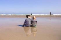 Girl sitting on beach with arm around brother — Stock Photo