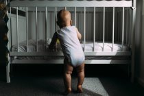 Garçon debout par lit bébé dans la chambre — Photo de stock